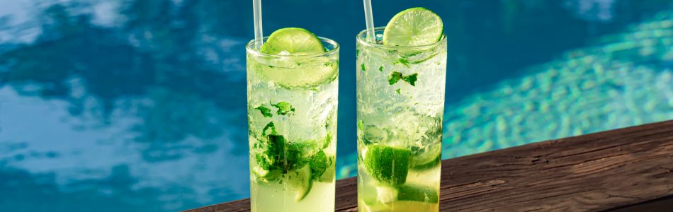 Two fresh and cool mojitos with ice cubes, lime slices and mint leaves on a turquoise pool background